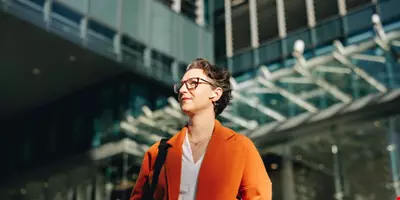 Low angle view of a mature businesswoman listening to music on earphones while commuting to work in the city. Thoughtful businesswoman walking to her office in the morning.